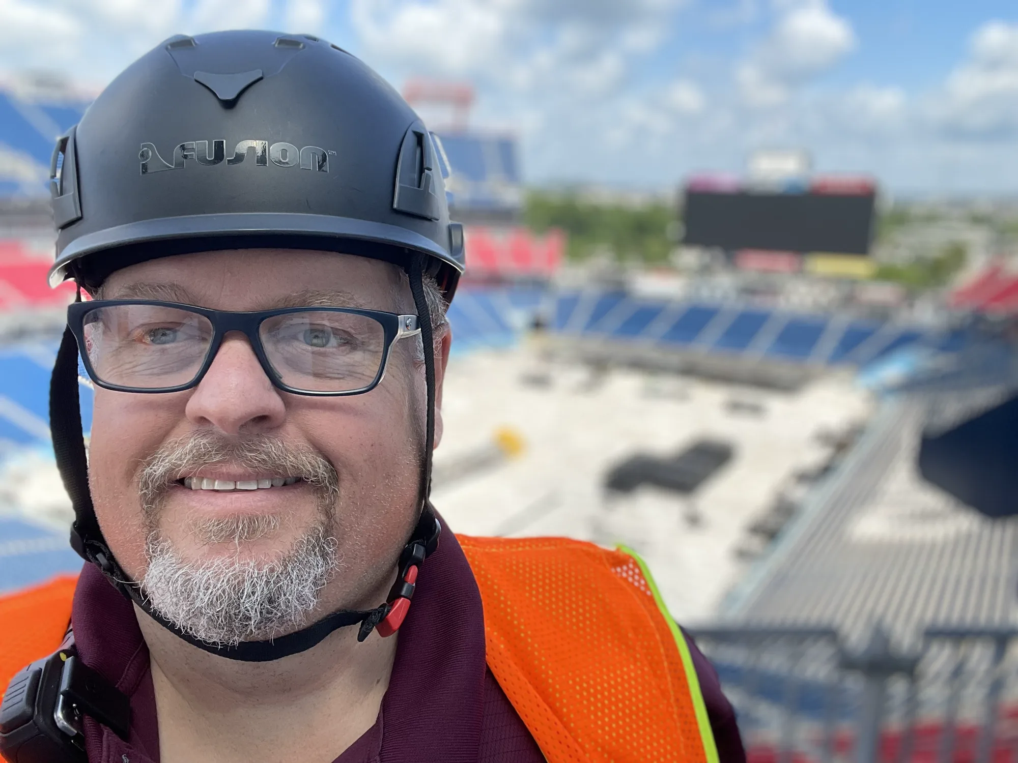 Earl Neal in a hard hat and safety vest high in a stadium during a load in